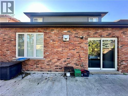 Brick exterior with a concrete patio, white-framed windows, and a sliding glass door - 5 Arden Avenue, Hamilton, ON 