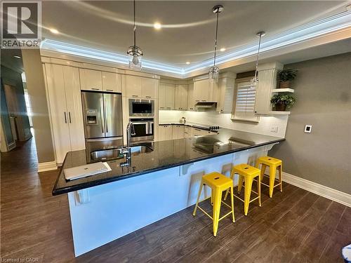 Gourmet kitchen featuring stainless steel appliances, dark stone countertops, wood-finish flooring, white subway tile backsplash, and recessed lighting - 5 Arden Avenue, Hamilton, ON 