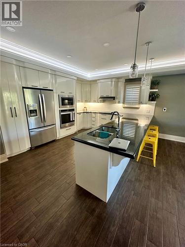 Kitchen featuring dark wood-finish flooring, white cabinetry, dark countertops, a stainless steel refrigerator, and pendant lighting - 5 Arden Avenue, Hamilton, ON 