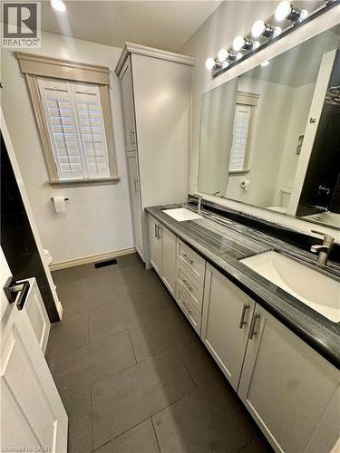 Dual vanity with integrated sinks, stone-finish countertop, white cabinetry with brushed nickel hardware, built-in tall linen cabinet, and plantation shutters - 5 Arden Avenue, Hamilton, ON 