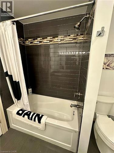 Bathtub with a shower fixture, dark subway tile surround, and decorative mosaic tile accent band - 5 Arden Avenue, Hamilton, ON 
