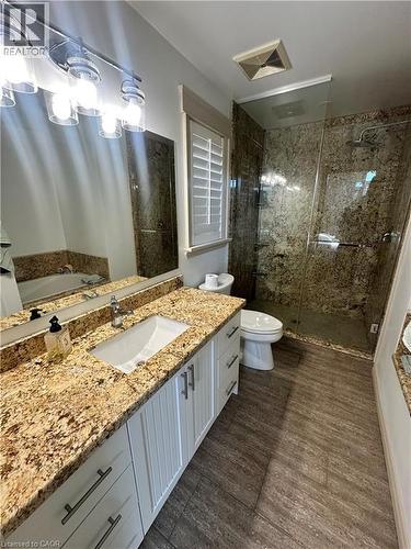 Dual vanity with stone countertops and undermount sinks, white shaker-style cabinetry, and wood-finish flooring - 5 Arden Avenue, Hamilton, ON 
