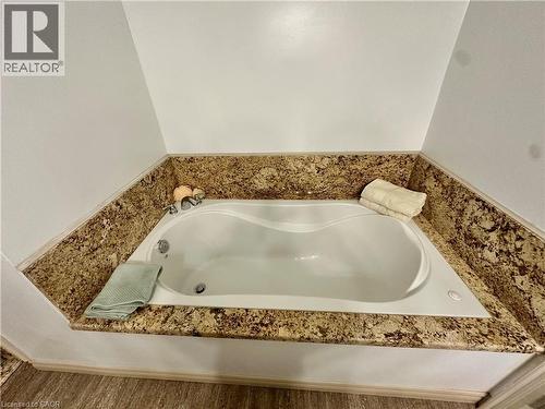 Built-in soaking tub with a stone-finish surround, wall-mounted fixtures, and wood-finish flooring - 5 Arden Avenue, Hamilton, ON 