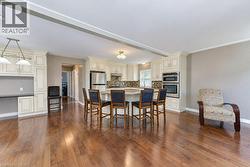 Hardwood flooring throughout, kitchen featuring cream-colored cabinetry, stainless steel appliances, a tile backsplash, and a multi-level breakfast bar - 