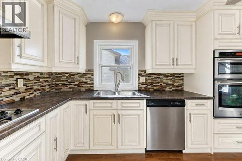 Kitchen featuring extensive upper and lower cabinetry, stainless steel appliances, a tile backsplash, and a double basin sink - 34 Wayne Drive, Kitchener, ON 