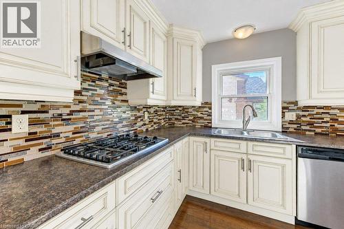 Kitchen featuring cream-colored cabinetry, a tile backsplash, dark countertops, a stainless steel gas range with a coordinating hood, and a double basin sink - 34 Wayne Drive, Kitchener, ON 