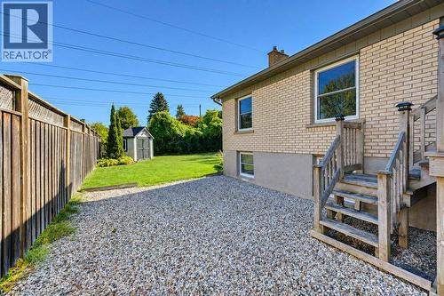 Manicured backyard featuring a storage shed, wood fence, gravel patio, and exterior wood stairs - 34 Wayne Drive, Kitchener, ON 