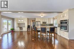Bright open-concept kitchen with wood-finish flooring, light-toned cabinetry, stainless steel appliances, and a central island with a stone-finish countertop - 