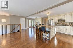 Hardwood flooring throughout, kitchen island with seating, stainless steel refrigerator, white cabinetry, and French doors - 