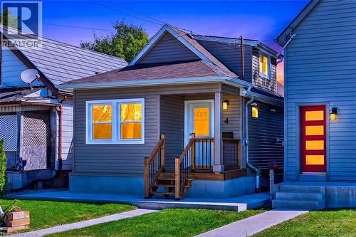 Curb appeal featuring a covered front porch, an exterior light fixture, and a wooden staircase with black railings - 4 Albemarle Street, Hamilton, ON 