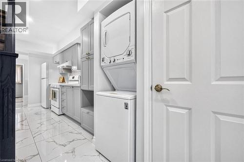 Compact kitchen featuring light gray cabinetry, white appliances, and a stackable washer and dryer unit - 4 Albemarle Street, Hamilton, ON 