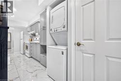 Compact kitchen featuring light gray cabinetry, white appliances, and a stackable washer and dryer unit - 