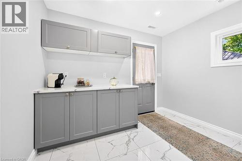 Gray shaker-style cabinetry with gold-tone hardware, white countertop, white tile flooring with gray veining, recessed ceiling lighting, and a white-framed window - 4 Albemarle Street, Hamilton, ON 