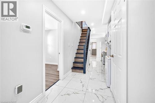 White tile flooring, wood-finish stairs with dark railing, white walls, and a visible doorway - 4 Albemarle Street, Hamilton, ON 