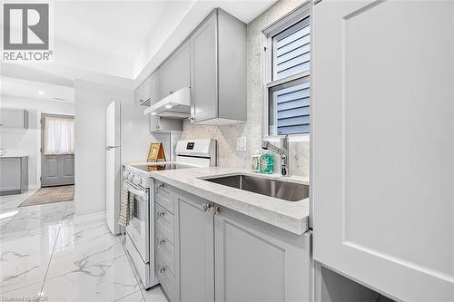 Light gray cabinetry with brushed nickel hardware, white stone countertops, stainless steel undermount sink, white tile flooring with gray veining, and white appliances - 4 Albemarle Street, Hamilton, ON 