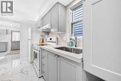 Light gray cabinetry with brushed nickel hardware, white stone countertops, stainless steel undermount sink, white tile flooring with gray veining, and white appliances - 