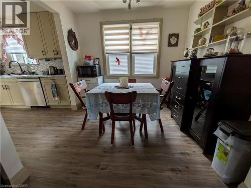 Kitchen area featuring wood-finish flooring, light-toned cabinetry, a stainless steel dishwasher, and a patterned tile backsplash - 487 Scholfield Avenue N, Welland, ON 