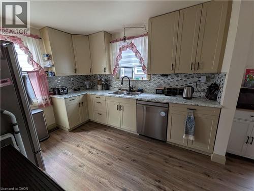 Kitchen featuring L-shaped cabinetry, wood-finish flooring, a tile backsplash, and a built-in stainless steel dishwasher - 487 Scholfield Avenue N, Welland, ON 