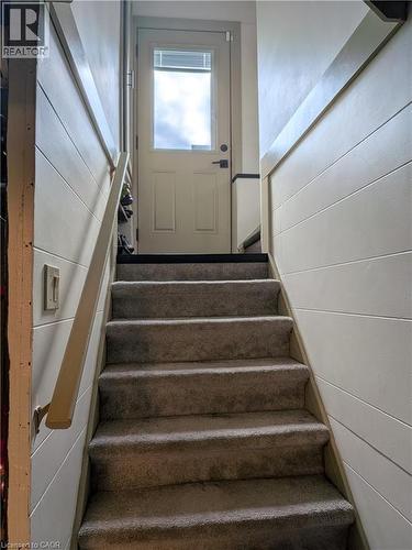 Carpeted staircase with a wood handrail, leading to an exterior door with a glass panel, flanked by paneled walls - 487 Scholfield Avenue N, Welland, ON 