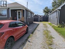 Exterior featuring dark siding, white trim, a covered front entry, and a gravel driveway leading to two detached garages - 