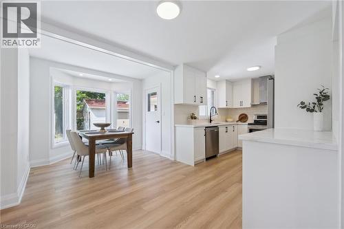 Open-concept kitchen and dining area featuring light wood-finish flooring, a kitchen with white cabinetry and stainless steel appliances, a white tile backsplash, and a dining space with a prominent b - 299 Dale Crescent, Waterloo, ON 