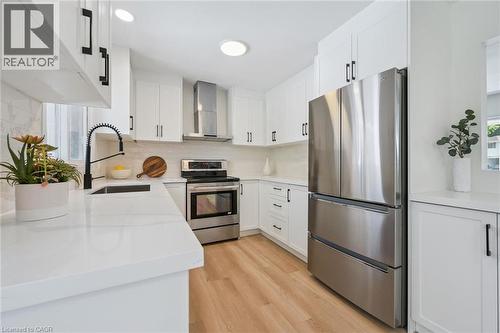Modern kitchen featuring white cabinetry, stainless steel appliances, light wood-finish flooring, white countertops, and a subway tile backsplash - 299 Dale Crescent, Waterloo, ON 