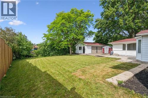 Expansive backyard featuring a large grass area, mature trees, a detached two-car garage with red roofing, a single-car garage, and a concrete patio - 299 Dale Crescent, Waterloo, ON 