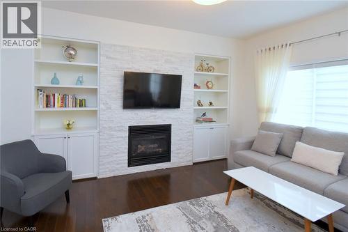 Bright, open living room featuring a white brick fireplace with built-in shelving and cabinetry, wall-mounted flat-screen television, wood-finish flooring, and abundant natural light from multiple win - 25 Guest Street, Hamilton, ON 
