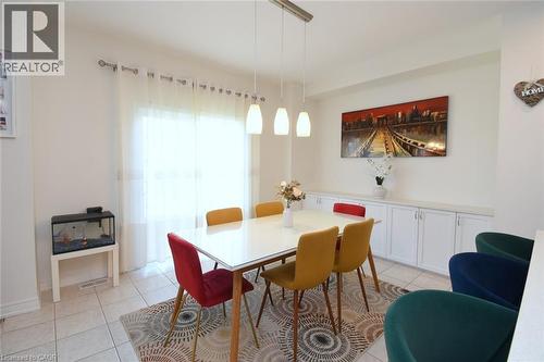 Recessed built-in cabinetry with white doors and a light-toned countertop, modern pendant light fixture, tiled flooring, expansive window with sheer curtains, and light-toned walls - 25 Guest Street, Hamilton, ON 