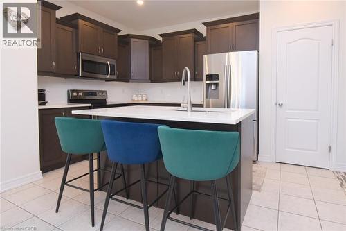 Kitchen featuring dark wood-finish cabinetry, white countertops, stainless steel appliances, a center island with sink, and light-toned tile flooring - 25 Guest Street, Hamilton, ON 