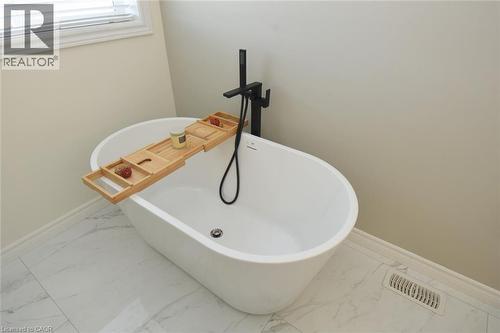 Freestanding soaking tub with a matte black floor-mounted faucet and handheld shower sprayer - 25 Guest Street, Hamilton, ON 