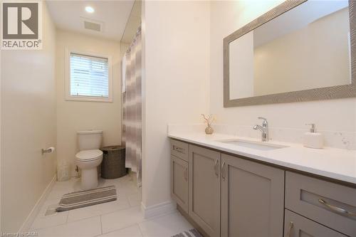 Rectangular mirror with textured frame, single basin vanity with white countertop, chrome faucet, shaker-style cabinetry, and white tile flooring - 25 Guest Street, Hamilton, ON 