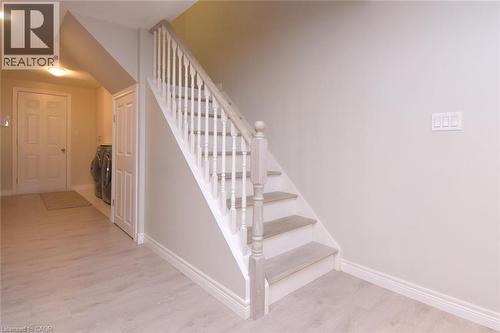 Staircase with painted risers and wood-finish treads, light-toned wood-finish flooring, and a paneled interior door - 25 Guest Street, Hamilton, ON 