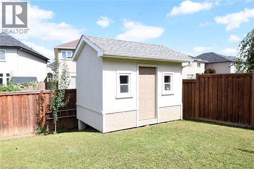 Detached storage shed with dual windows and a paneled door, set within a fenced yard featuring wood privacy fencing and a manicured lawn - 25 Guest Street, Hamilton, ON 