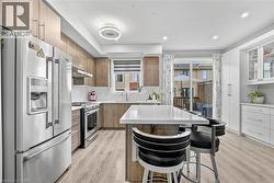 Contemporary kitchen featuring wood-finish cabinetry, stainless steel appliances, a white island countertop, and light wood-look flooring - 