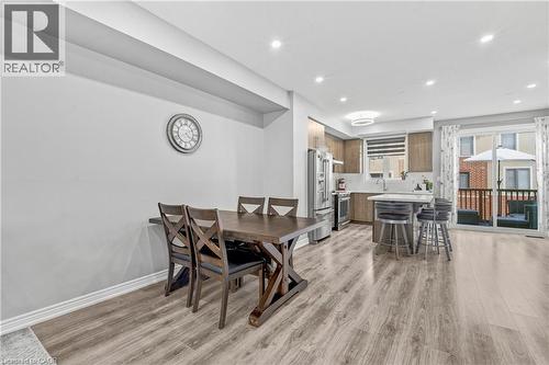 Open-concept living area with wood-finish flooring, recessed lighting, and a modern kitchen featuring stainless steel appliances, a center island with seating, and wood-finish cabinetry - 1890 Rymal Road E Unit# 144, Hamilton, ON 
