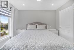 Bright secondary bedroom featuring a curved upholstered headboard, recessed ceiling lighting, large windows with motorized roller shades, and direct access to a covered outdoor balcony overlooking the - 