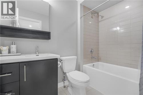 White undermount sink with a chrome faucet, dark wood-finish vanity with chrome hardware, rectangular mirror, and a white bathtub with horizontal tile surround - 1890 Rymal Road E Unit# 144, Hamilton, ON 
