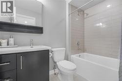 White undermount sink with a chrome faucet, dark wood-finish vanity with chrome hardware, rectangular mirror, and a white bathtub with horizontal tile surround - 