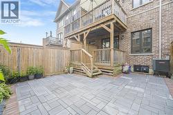 Paved patio area, wooden privacy fencing, multistory wooden deck, brick exterior, and multiple large windows - 