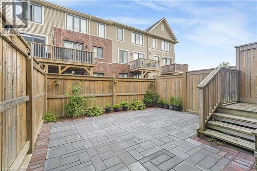 Private patio featuring paver stones with brick-finish border, wood fencing, and wood stairs leading to an elevated deck - 1890 Rymal Road E Unit# 144, Hamilton, ON 