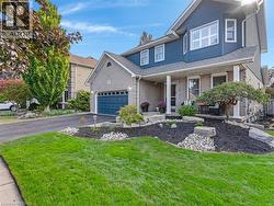 Exterior featuring blue siding, light grey brick, a covered front porch, an integrated two-car garage with a blue door, and established landscaping - 