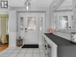 White tile flooring, wainscoting detail, front entry door with decorative glass inserts, and a clear glass pendant light fixture - 