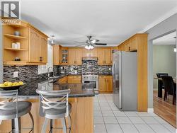 Kitchen featuring wood cabinetry, dark stone countertops, stainless steel appliances, a mosaic tile backsplash, and white tile flooring - 