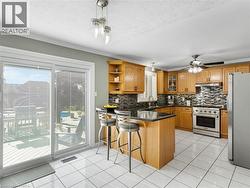 Kitchen featuring wood cabinetry, stainless steel appliances, black countertop, tile backsplash, and white tile flooring - 