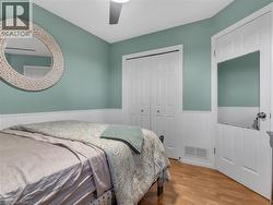 Wood-finish flooring, white paneled wainscoting, white bi-fold closet doors, and an overhead ceiling fan - 