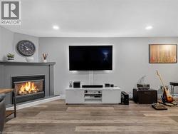 Gas fireplace with a gray mantel, recessed lighting, wood-finish flooring, and a built-in media console - 