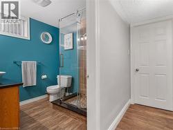 Glass-enclosed shower with pebble-finish flooring, wood-finish flooring, wood vanity, and a window with blinds - 