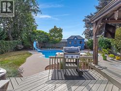 Expansive backyard featuring a built-in swimming pool with a slide, substantial decking, a blue accessory building, and mature perimeter landscaping - 