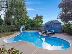 Curved inground pool with a slide, concrete pool deck, and a detached blue accessory structure - 